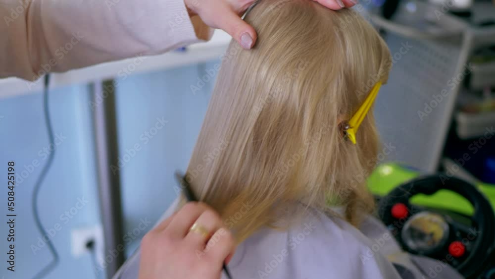 Little girl gets a haircut in a children's barbershop. Beautiful girl, blonde.