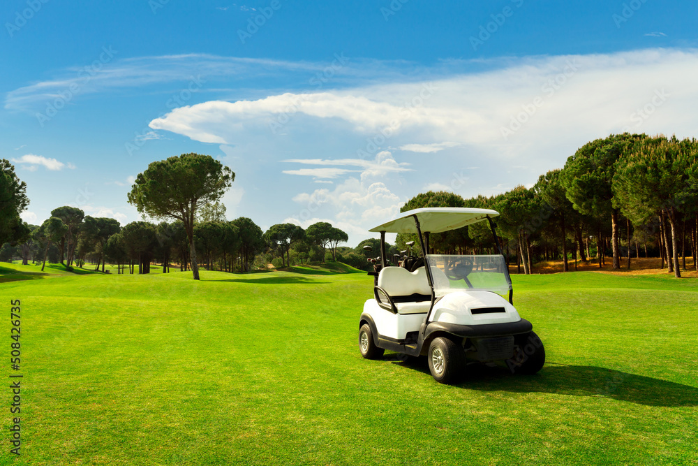 Fototapeta premium Golf cart in fairway of golf course with green grass field with cloudy sky and trees at sunset