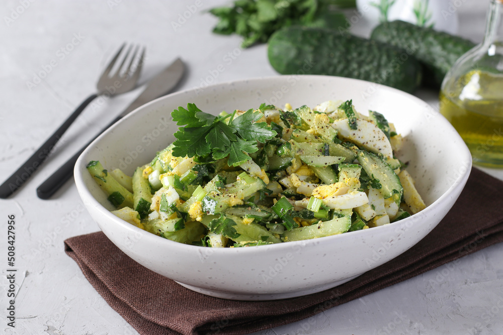 Salad with squid, cucumber, egg and green onion dressed with olive oil in a white bowl on light gray background Salad with squid, cucumber, egg and green onion dressed with olive oil in a white bowl on light gray background