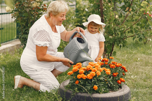 Little girl and her grandmother watering flowers in garden