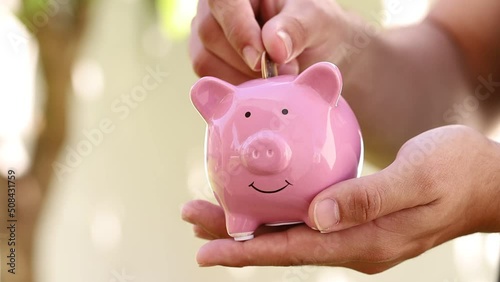 Um homem colocando moedas do Real - BRL, dinheiro do Brasil, dentro de um cofrinho de porco mealheiro. Conceitos de guardar dinheiro, finanças e investimentos. photo