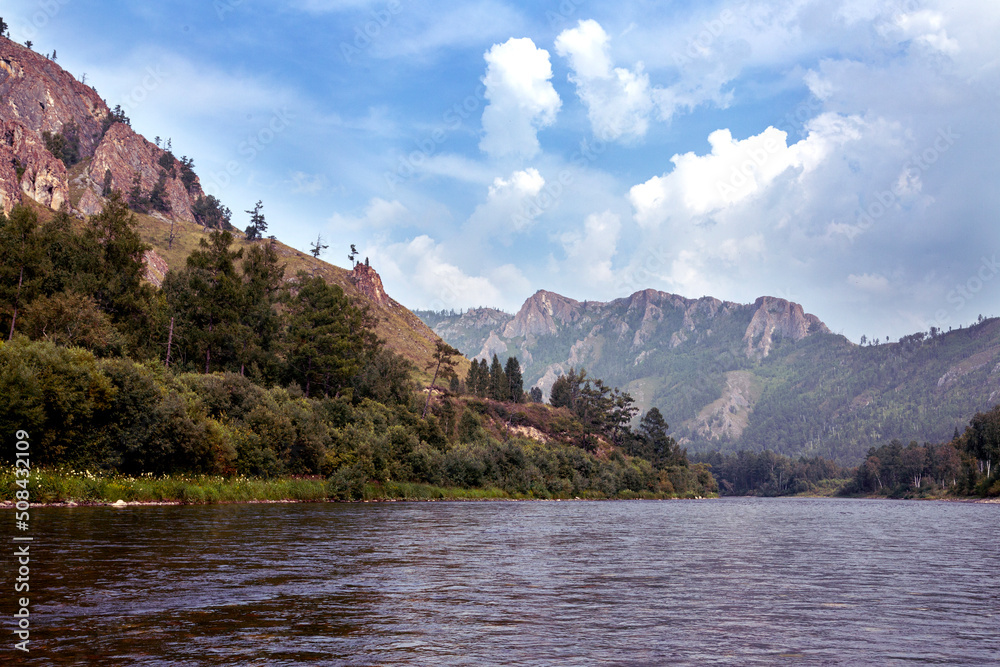 A river and forested mountains along its banks. Summer landscape. Travel, hiking, healthy lifestyle.
