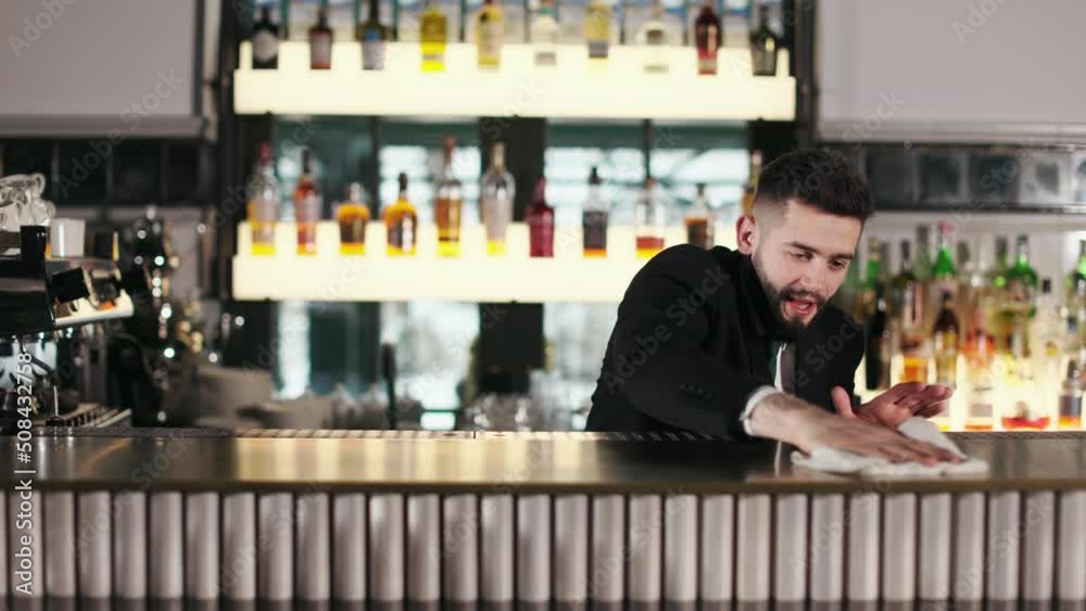 Caucasian bearded barman in uniform wiping wooden surface of bar ...