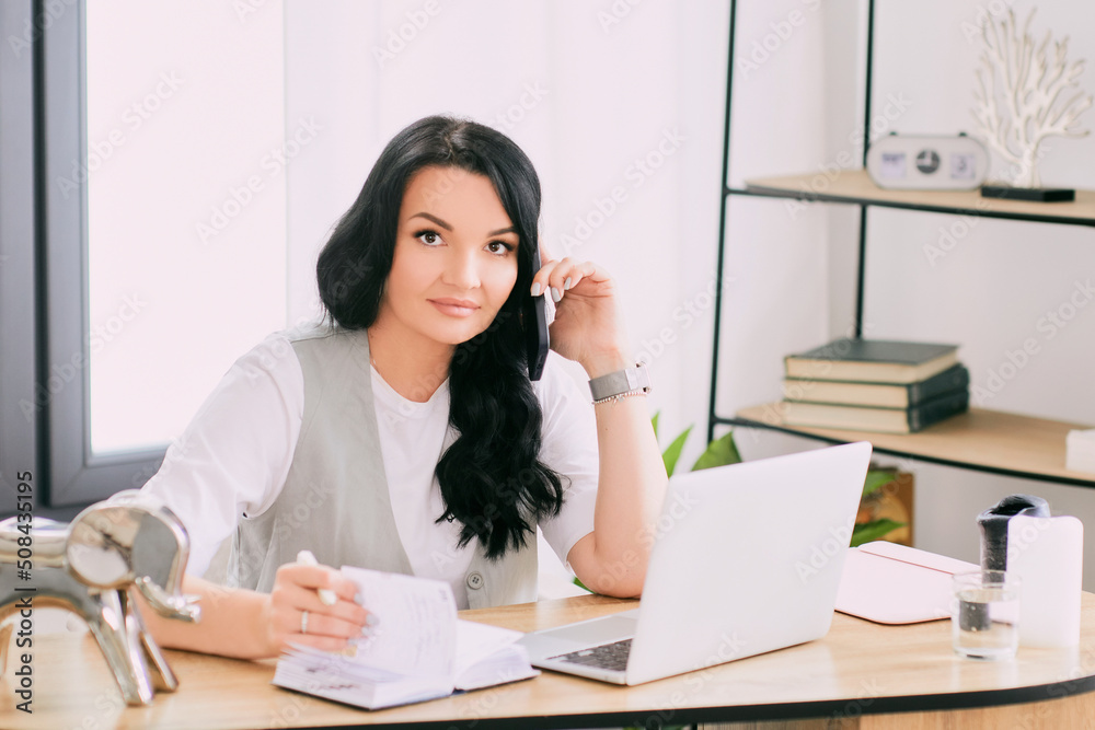 woman entrepreneur talking on cellphone and making notes in her notebook. Business, analytics, education woman entrepreneur talking on cellphone and making notes in her notebook. Business, analytics, education