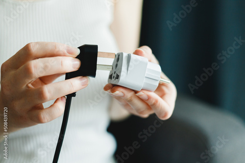 Woman applies universal travel adapter electrical plug converter power socket photo