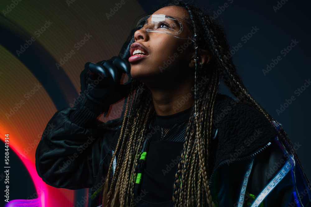Naklejka premium Stylish african american woman in cyber glove and smart glasses standing on grey background with abstraction.