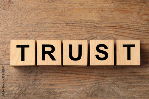 Cubes with word TRUST on wooden table, flat lay
