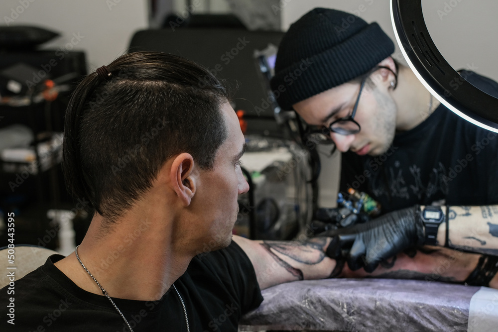 Professional tattoo artist stuffs a tattoo on the man's hand. Tattoo artist at work. Tattoo creation process. Art and creativity Professional tattoo artist stuffs a tattoo on the man's hand. Tattoo artist at work. Tattoo creation process. Art and creativity