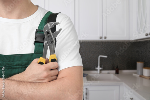 Plumber with pipe wrench in kitchen, closeup. Space for text photo