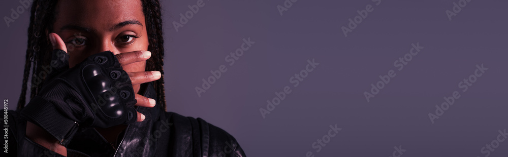 African american woman in glove covering face isolated on purple, banner.