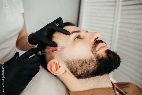 Beauty treatments for a stylish young man with a beard. Beautician makes beauty injections in a man's face