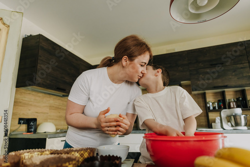 mom with her little sons at the table in the kitchen at home preparing together the dough for baking a holiday cake photo