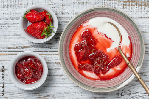 Plate with red strawberries and natural yogurt on a wooden table, top view