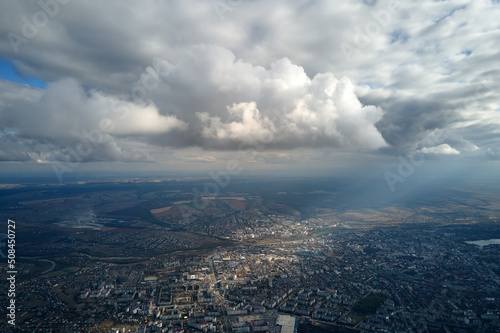 Aerial view from airplane window at high altitude of distant city covered with puffy cumulus clouds forming before rainstorm