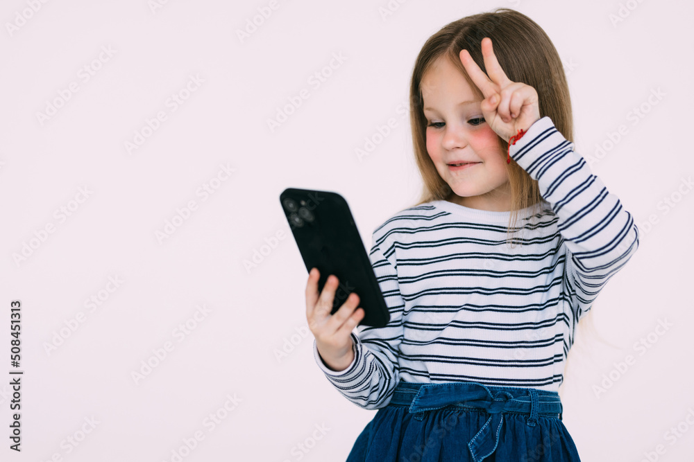 Surprised happy cute blond teenage little b-day girl receive congratulations via video-call, smiling amazed hold smartphone raise hand excited and amused, look mobile phone joyful, white background