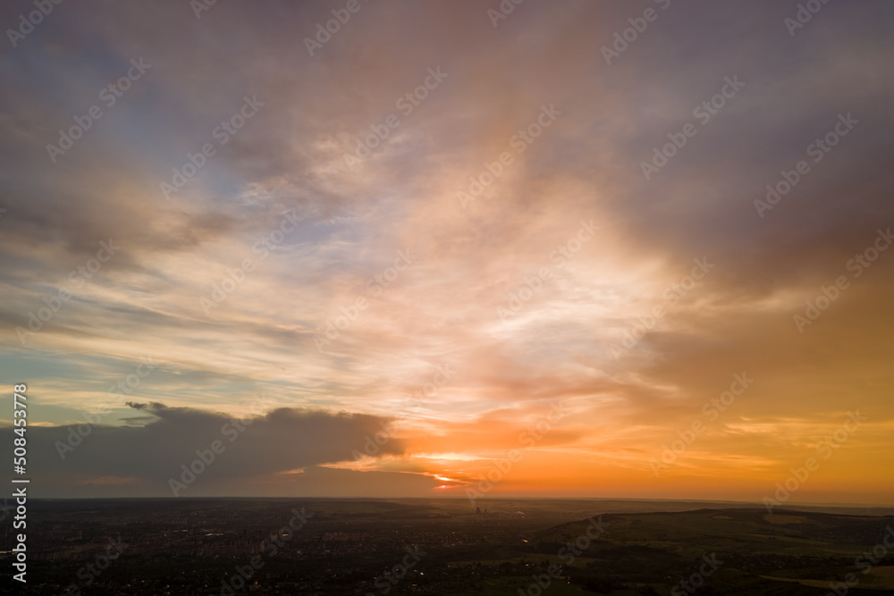 Bright colorful sunset sky with setting sun and vibrant clouds over dark landscape