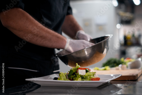 chef cook hands in gloves prepare or put healthy greek salad on plate at kitchen