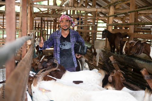 A positive farmer is happy between his pets. A male farmer in a goat farm smiles as he looks at the goats in the farm.