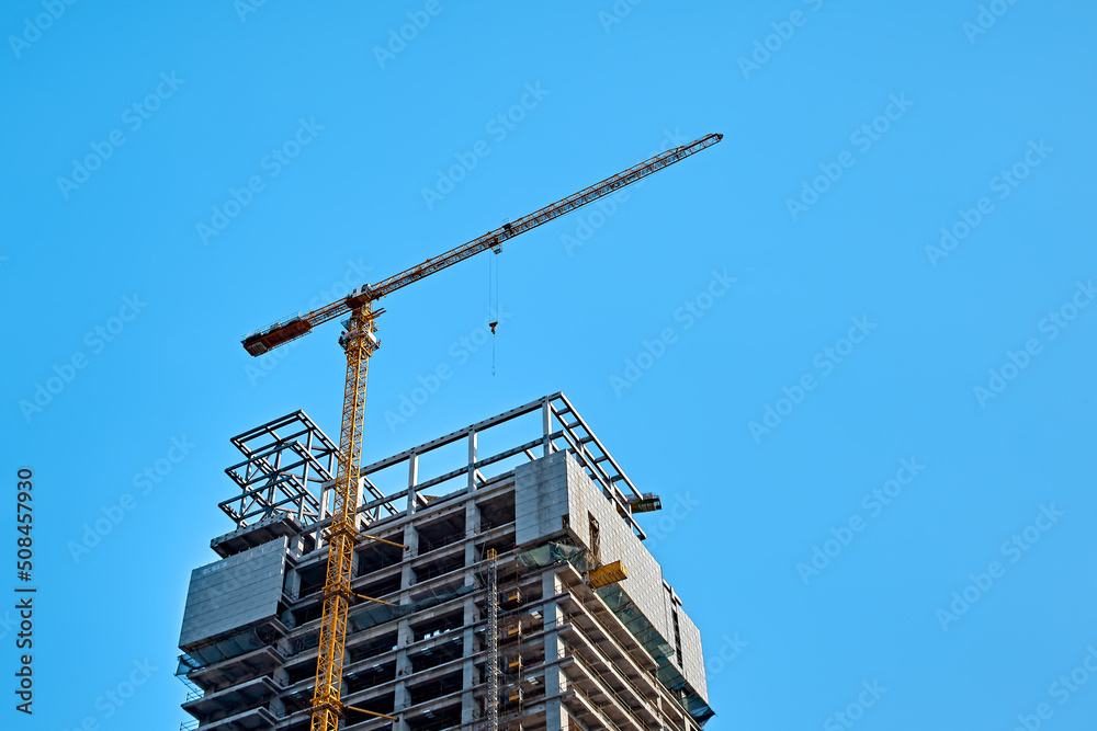 Top of yellow tower crane on skyscraper construction against clear blue sky, bottom view Top of yellow tower crane on skyscraper construction against clear blue sky, bottom view