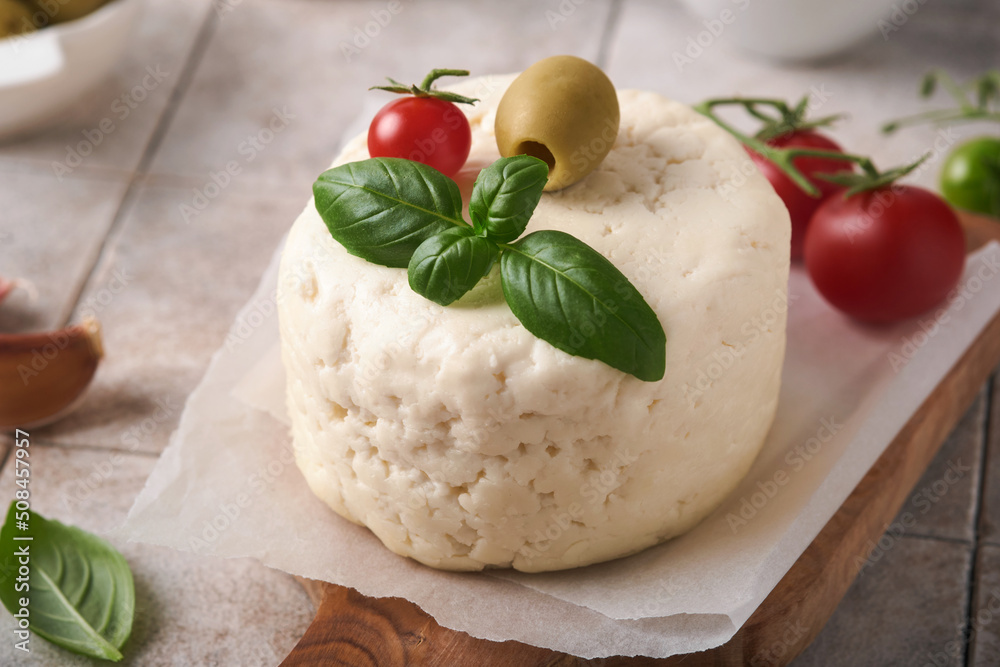 Ricotta cheese. Homemade Ricotta cheese with basil, garlic, tomatoes and green olives on parchment paperback and stand on old beige tiles background. Italian food. Selective focus.