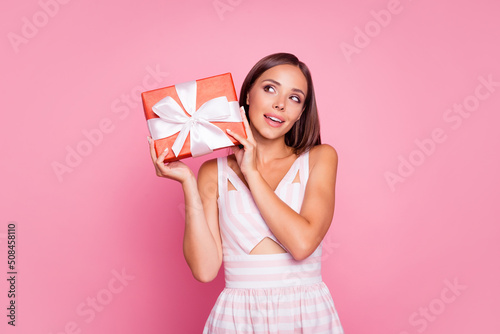 Photo of shiny thoughtful young lady dressed summer clothes holding gift looking empty space isolated pink color background