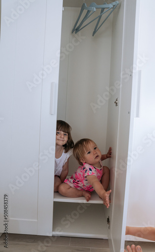 Two little girls looking out of white wardrobe