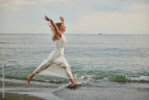 a girl in a white dress jumps on the shore