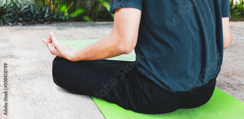 Young Asian man practicing yoga  breathing  meditation  adha exercise  padmasana  half lotus pose with mud pose on the green yoga mat. Exercise in the garden.Healthy living concept.
