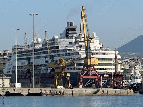 Passenger ship in harbor with cranes and city background