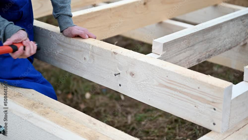 Man worker building wooden frame house. Carpenter hammering nail into wooden board, using hammer. Carpentry concept. Man worker building wooden frame house. Carpenter hammering nail into wooden board, using hammer. Carpentry concept.