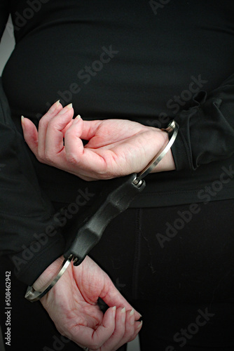 A woman being arrested and standing with her hands in handcuffs behind her back. The arrested prisoner is facing the wall.