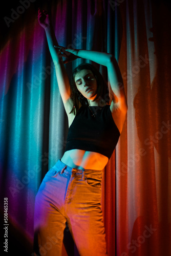 Young and sexy woman with wearing jeans and black t-shirt posing in colorful neon light