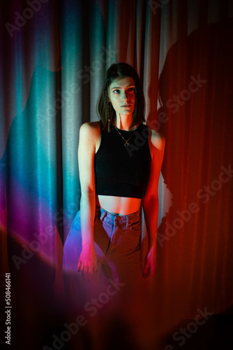 Young and sexy woman with wearing jeans and black t-shirt posing in colorful neon light