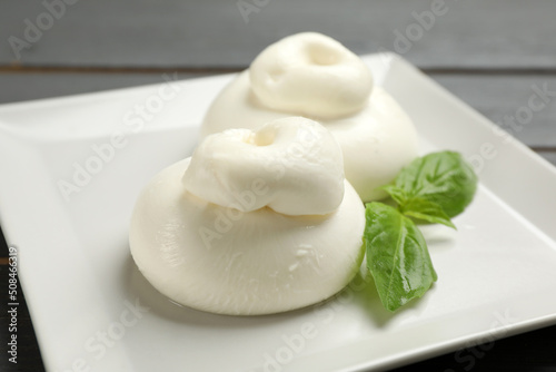 Delicious burrata cheese with basil on table, closeup