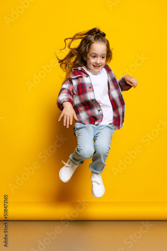 Happy little girl, kid wearing warm plaid shirt having fun isolated on bright yellow background. Concept of children emotions, fashion, beauty, school and ad concept