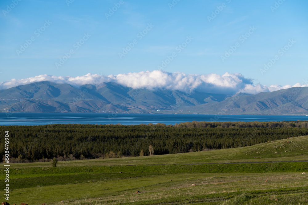 Beautiful summer landscape. Green fields forest, blue lake and mountains under the clouds.