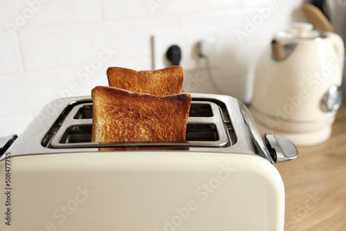 Modern white toaster and roasted bread slices toasts inside on wooden table in kitchen
