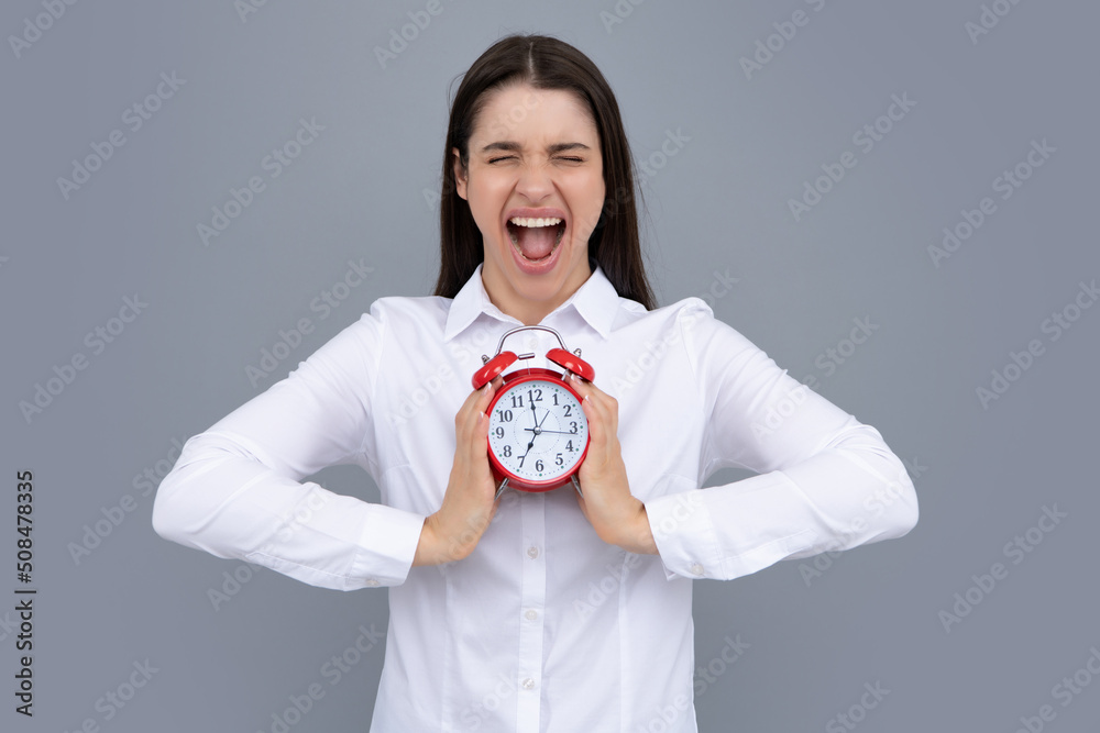 Woman holds a clock. Emotional young female face. Portrait of young surprised woman with alarm clock on grey background. Woman holds a clock. Emotional young female face. Portrait of young surprised woman with alarm clock on grey background.