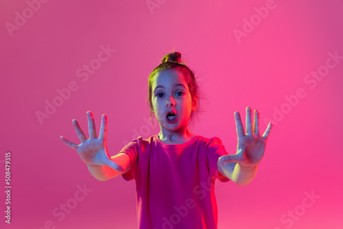Scared little girl  kid wearing pink t-shirt posing isolated on magenta color background. Concept of children emotions  fashion  beauty  school and ad concept