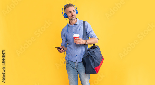 handsome businessman in headphones use smartphone with travel bag. man listen music