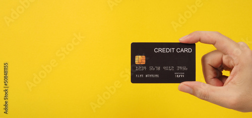 Hand is holding black credit card on yellow background. photo