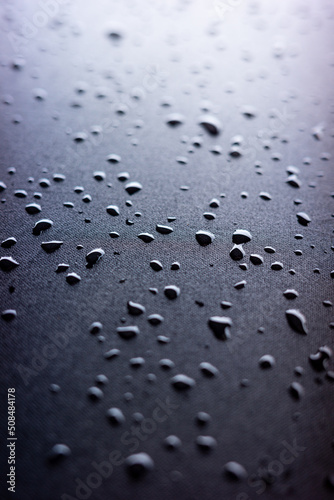Selective focus on water drops on black synthetic fabric.