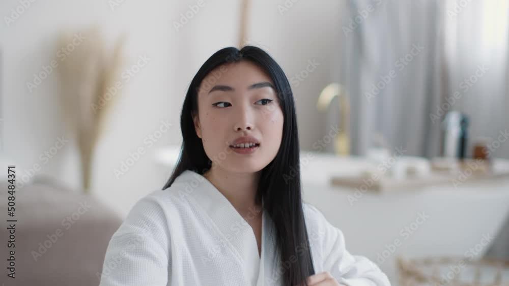 Haircare rituals. Young pretty asian lady combing her healthy hair in home, sitting at bathroom in morning, free space Haircare rituals. Young pretty asian lady combing her healthy hair in home, sitting at bathroom in morning, free space