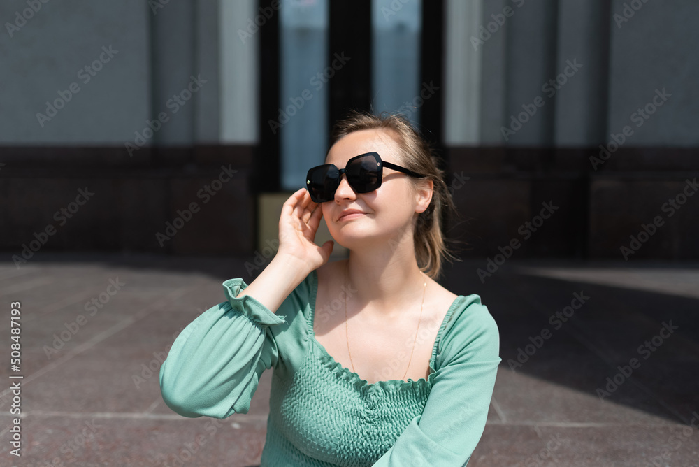 Fototapeta premium A blonde woman in sunglasses and a green blouse on the street in the summer