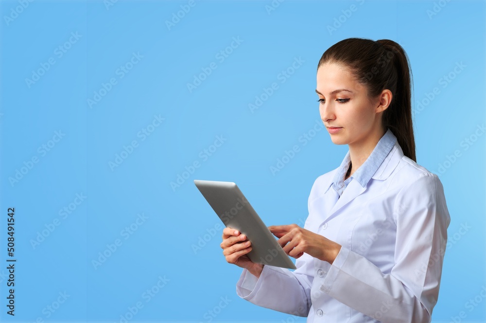 Beautiful young girl doctor, with digital table on a blue background. Medical student practitioner. The concept of medical education Beautiful young girl doctor, with digital table on a blue background. Medical student practitioner. The concept of medical education