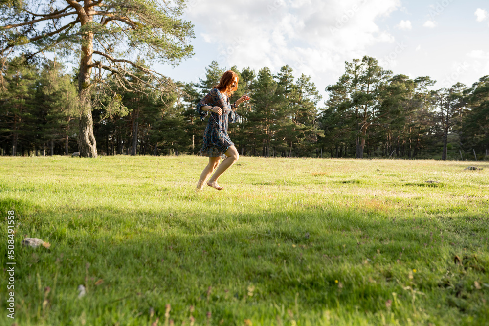 Fototapeta premium Beautiful middle-aged woman enjoying summer outdoor activities, running through the meadow. Happy and joyful 50 years old woman leading a healthy lifestyle.