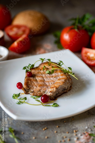 A hearty lunch, a romantic dinner. Grilled French steak with thyme and cranberries on a beautiful white plate on a gray background. Vertical photo. Close-up.