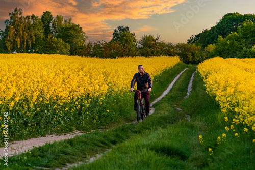 man rides a bike through the countryside. Road through the yellow field