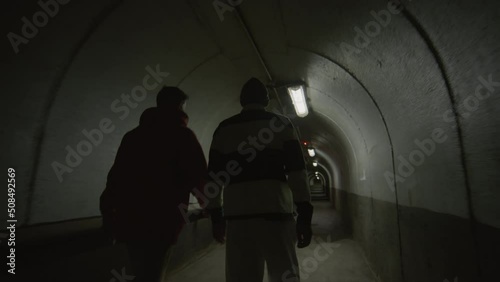 Following shot of two boys in streetwear walking through dark concrete tunnel with red light, giving each other fist bump and chatting after practicing parkour photo