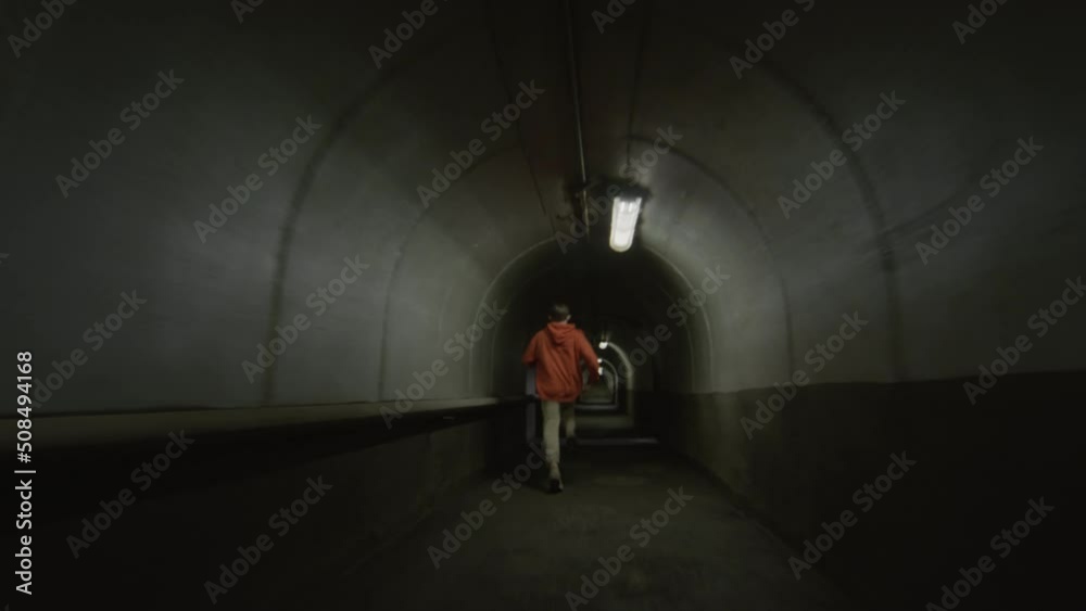 Dolly shot of two parkour athletes passing by each other while running through dark concrete tunnel with flickering red light Dolly shot of two parkour athletes passing by each other while running through dark concrete tunnel with flickering red light